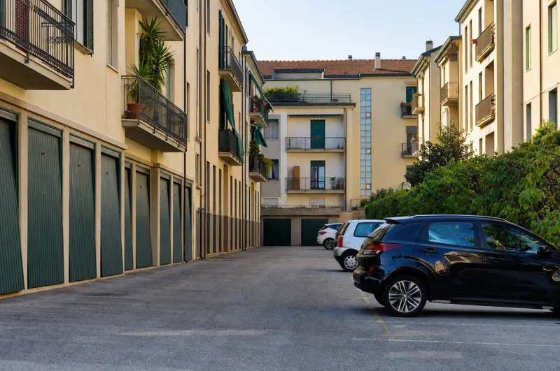 La fila dei box di un condominio lungo il cortile, con le auto nei posti assegnati.