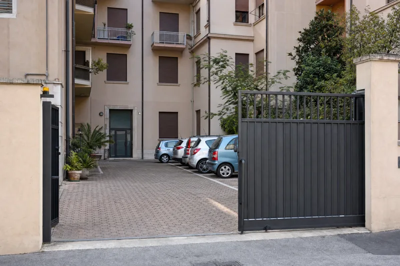 Il cancello scorrevole di un condominio, aperto sul cortile con i posti auto.