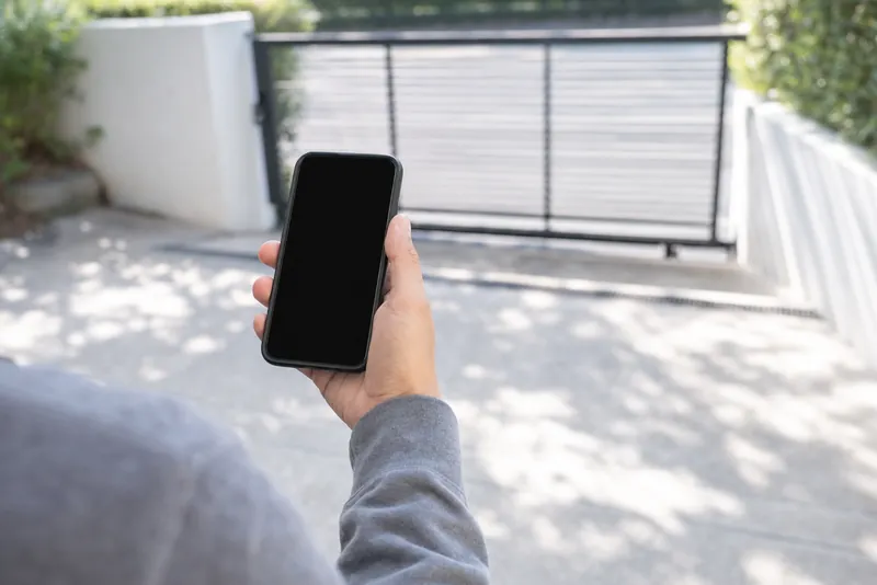 Una mano con lo smartphone, il cancello sfocato dietro.